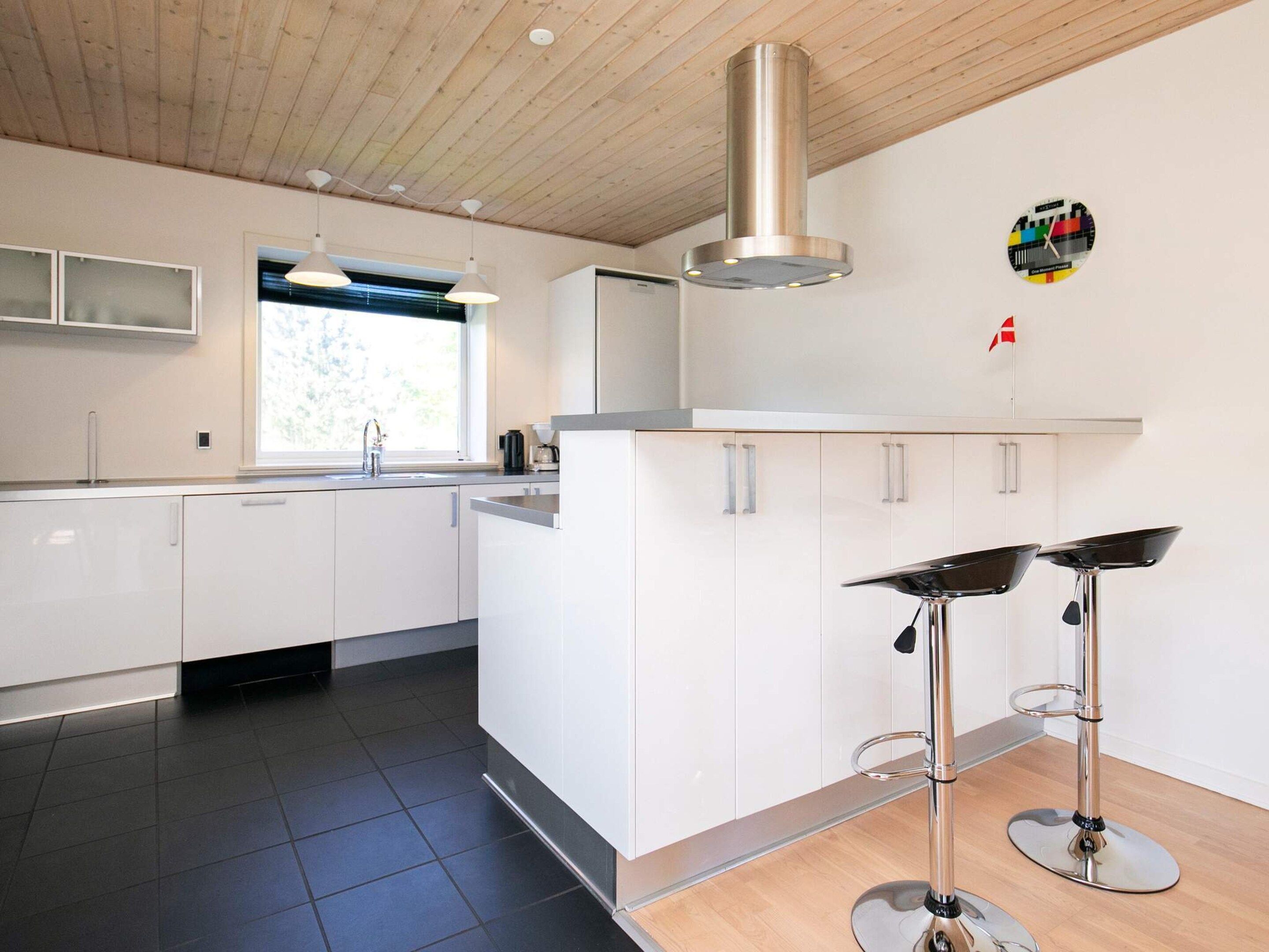 A modern kitchen with white cabinets, a stainless steel range hood, a window with a view, and two bar stools.