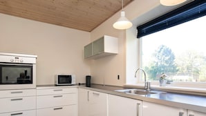 Eine moderne Küche mit weißen Schränken, einem eingebauten Ofen, einer Mikrowelle, einem Spülbecken und einem Fenster mit Blick auf Bäume.