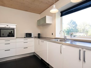 Una cucina moderna con mobili bianchi, forno a incasso, microonde, lavello e finestra vista alberi.