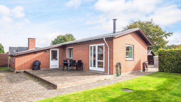 Ein Ziegelhaus mit Terrasse, Grill und überdachter Sitzgruppe.