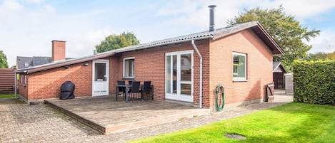 A brick house with a covered patio, a barbecue grill, and a small garden.