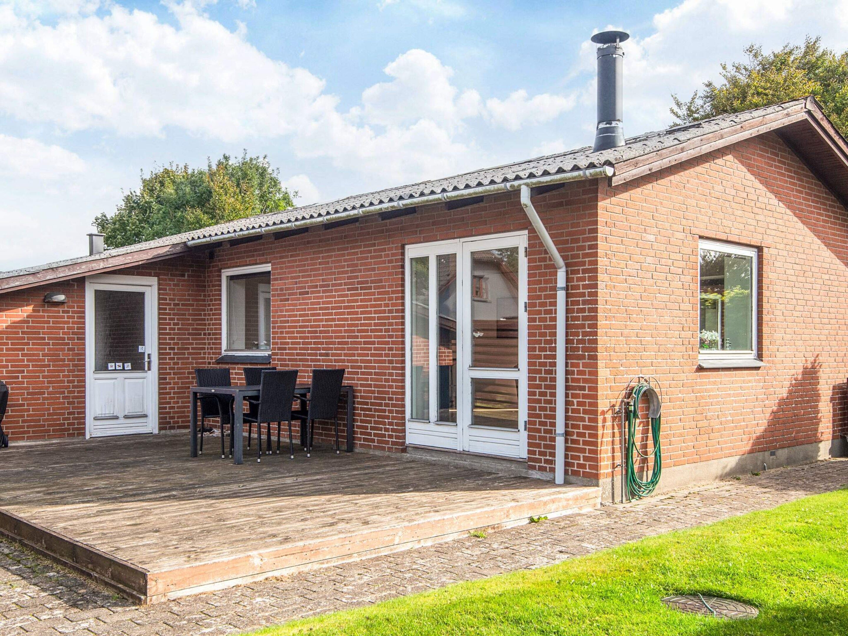 A brick building with a covered patio, a table with chairs, and a hose.