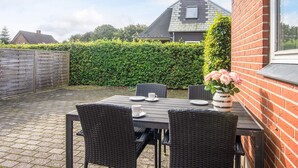 A patio with a table and chairs, a brick wall, and a hedge. - 4 Person Holiday Home in Oksbol (Oksbol)