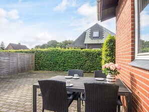 A patio with a table and chairs, a brick wall, and a hedge.