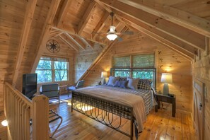 A cozy cabin bedroom with a bed, a chair, a TV, and a window with blinds.