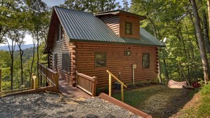 Uma cabana de toras com telhado de metal, deck de madeira e um pequeno alpendre.
