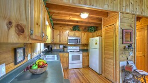 Cocina rústica con alacena de madera, pileta de acero inoxidable, estufa blanca y refrigerador.