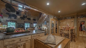 A rustic kitchen with wooden cabinets, a large island, and a staircase leading to a loft area. - Experience the allure of Roost on the Ridge a pet-friendly sanctuary with hot tub, firepit, ping pong, spacious screen porch, and WiFi (Ellijay)