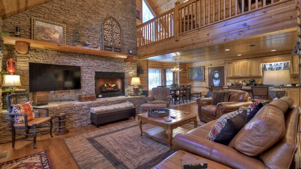 A spacious living room with a stone fireplace, leather sofas, and a high ceiling with wooden beams.