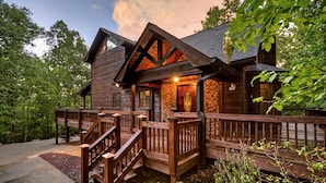 A log cabin with a stone foundation, wooden exterior, and a wooden deck with stairs leading to the entrance.