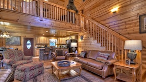 A spacious log cabin interior with a cozy living area, a kitchen, and a staircase.