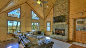 A spacious living room with a stone fireplace, leather sofa, and large windows. - Wakin on a Pretty Day: Luxurious pet-friendly retreat with stunning mountain views, hot tub, outdoor fireplace, pool table, WiFi, and downtown convenience (Blue Ridge)
