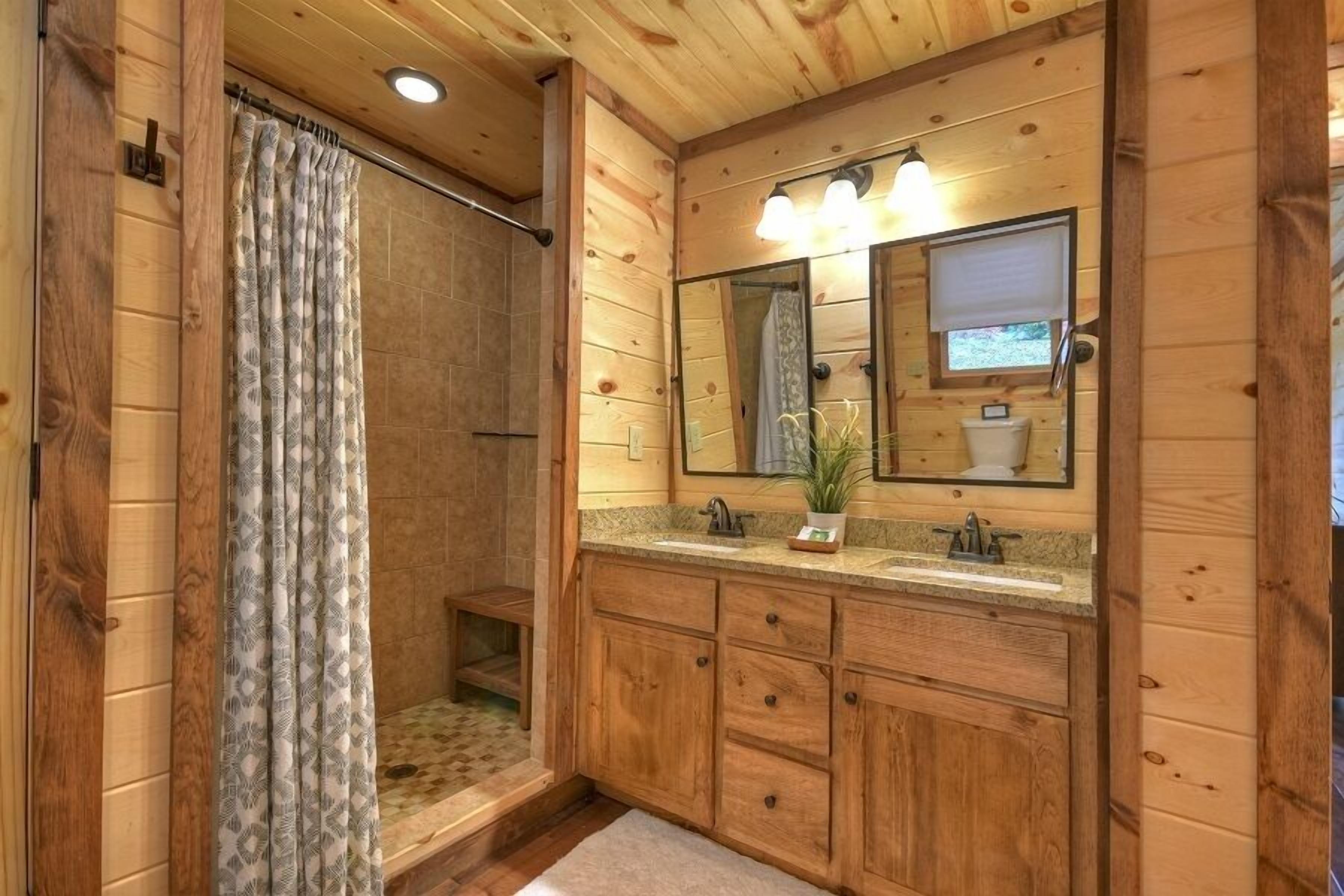 Baño de cabaña de madera con ducha, tocador y un espejo grande.