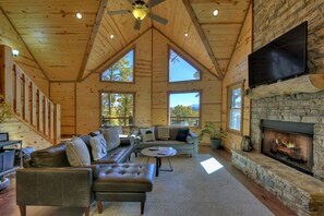 L’intérieur d’une cabane en rondins, avec une cheminée en pierre, des canapés en cuir et de grandes fenêtres.
