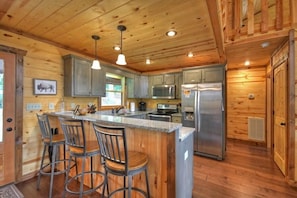A wooden cabin interior with a kitchen featuring a central island, bar stools, and modern appliances.