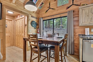 A wooden interior with a dining table, chairs, a clock, and a window with a view of trees. - Up, Up and Away is pet friendly with a beautiful mountain view, hot tub, firepit, WiFi and fenced yard (Blue Ridge)