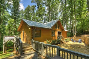 A cabin with a wooden deck, a covered porch, and a view of the surrounding forest.