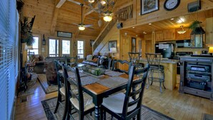A wooden cabin interior with a dining area, kitchen, and living room. - Ascend to serenity at Higher Ground! This pet-friendly haven offers majestic mountain views, a hot tub, firepit, WiFi, and unparalleled privacy. WiFi (Blue Ridge)