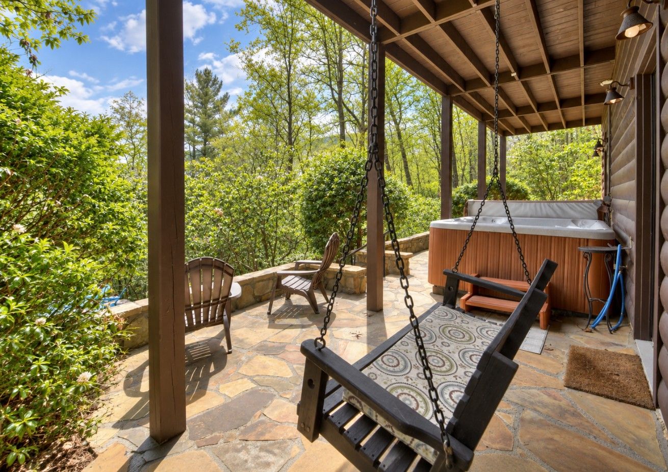 An outdoor patio with a swing chair, a wooden bench, and a hot tub.