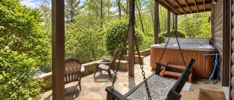 An outdoor patio with a swing chair, a wooden bench, and a hot tub.