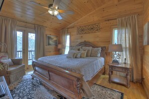 A wooden cabin bedroom with a large bed, a ceiling fan, and a window with curtains. - Ascend to serenity at Higher Ground! This pet-friendly haven offers majestic mountain views, a hot tub, firepit, WiFi, and unparalleled privacy. WiFi (Blue Ridge)