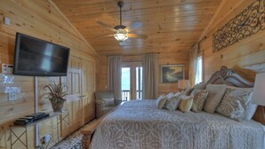 A wooden cabin bedroom with a large bed, a ceiling fan, a TV, and a potted plant. - Ascend to serenity at Higher Ground! This pet-friendly haven offers majestic mountain views, a hot tub, firepit, WiFi, and unparalleled privacy. WiFi (Blue Ridge)