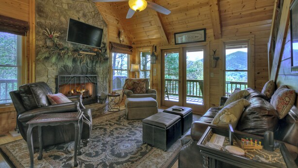 A cozy cabin interior with a stone fireplace, leather furniture, and a large window offering a mountain view. - Ascend to serenity at Higher Ground! This pet-friendly haven offers majestic mountain views, a hot tub, firepit, WiFi, and unparalleled privacy. WiFi (Blue Ridge)