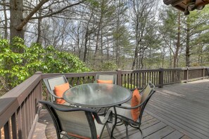 A round glass table with two chairs and orange cushions on a wooden deck. - Ascend to serenity at Higher Ground! This pet-friendly haven offers majestic mountain views, a hot tub, firepit, WiFi, and unparalleled privacy. WiFi (Blue Ridge)