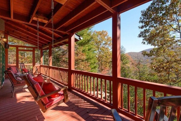 A wooden deck with red railings and a hanging chair. - Ascend to serenity at Higher Ground! This pet-friendly haven offers majestic mountain views, a hot tub, firepit, WiFi, and unparalleled privacy. WiFi (Blue Ridge)