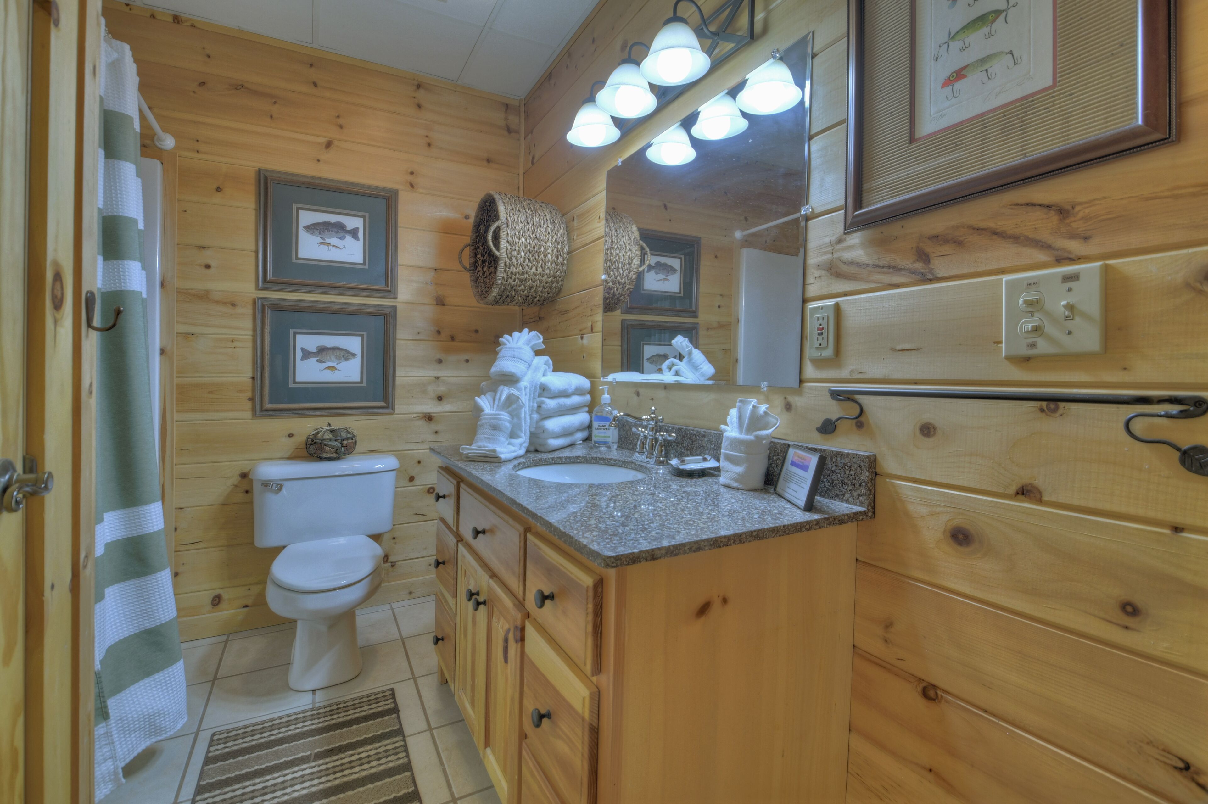 A wooden cabin bathroom with a toilet, sink, and vanity. There are framed pictures on the wall, a towel rack, and a mirror above the sink.