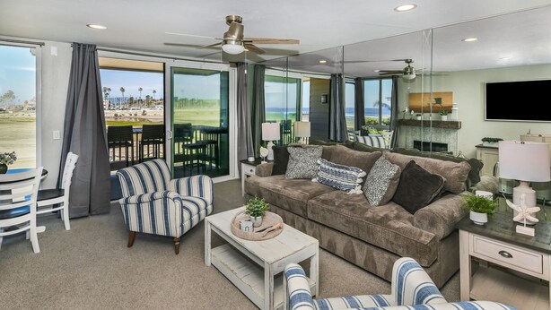 A spacious living room with a large window, a ceiling fan, a sofa, a striped armchair, and a coffee table. - F14 Upper Cottage, Amazing oceanviews/Beachfront Luxury, Triple queen bunk, North Coast Village (Oceanside)