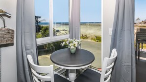A corner room with a view of the beach, a small table with a vase of flowers, and white chairs. - F14 Upper Cottage, Amazing oceanviews/Beachfront Luxury, Triple queen bunk, North Coast Village (Oceanside)