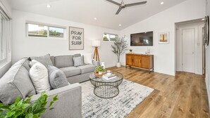 Un salon moderne avec un canapé gris, une table basse, un lampadaire, un téléviseur et un ventilateur de plafond.