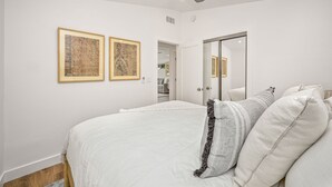 Une chambre à coucher comprenant un lit, deux œuvres d’art encadrées, un ventilateur de plafond et un miroir.