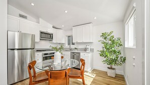 Une cuisine moderne avec des meubles blancs, des appareils en acier inoxydable et une table à manger en verre, assortie de chaises en bois.