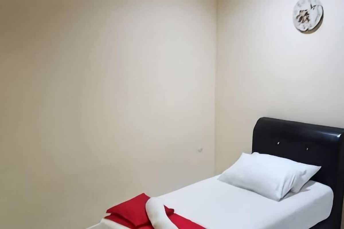 A single bed with a white mattress and red blanket, a black headboard, and a wall clock.