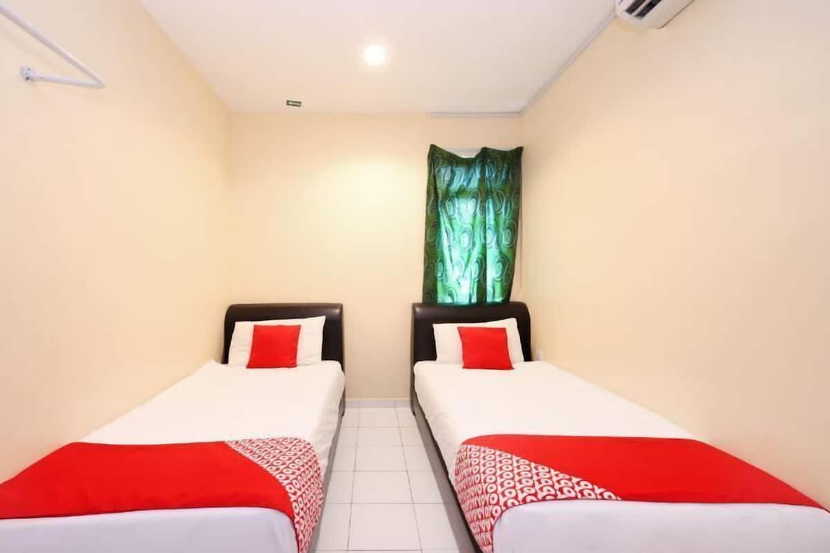 A small, clean room with two single beds, each with a red and white bedspread, and a green curtain on the window.