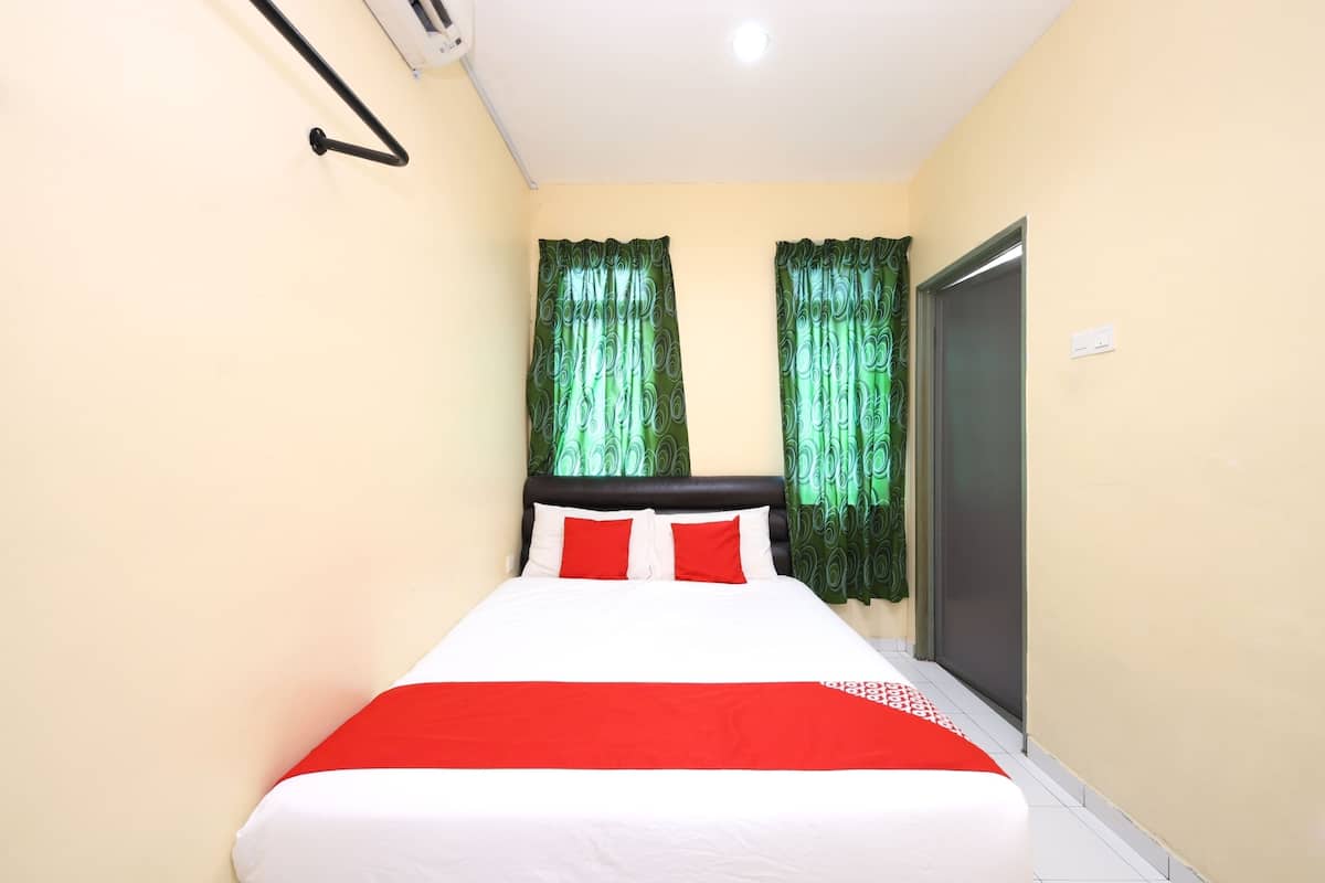 A neatly made bed with a red and white bedspread, two red pillows, and green patterned curtains.