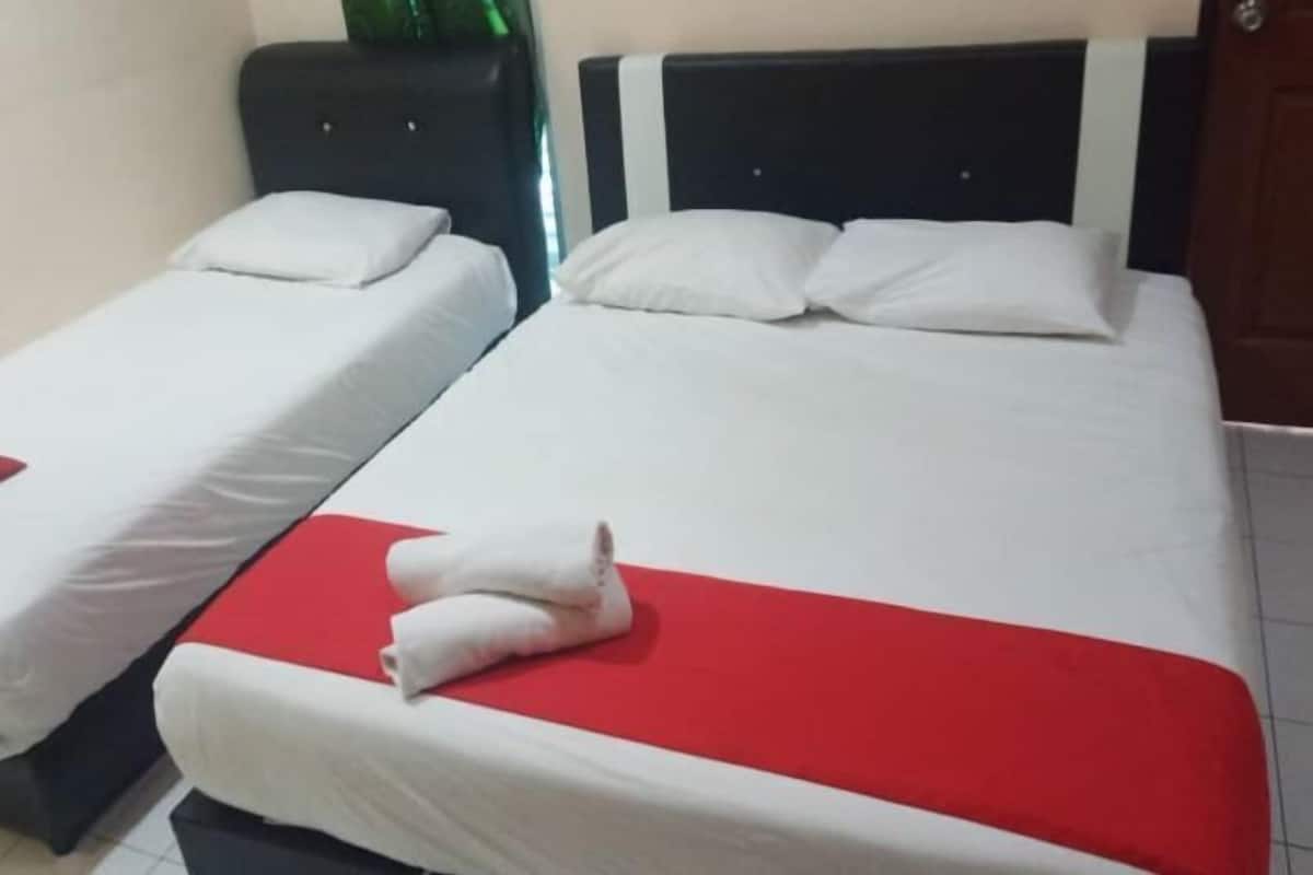 Two single beds with white bedding and red accents, a dark headboard, and a wooden door in a room.