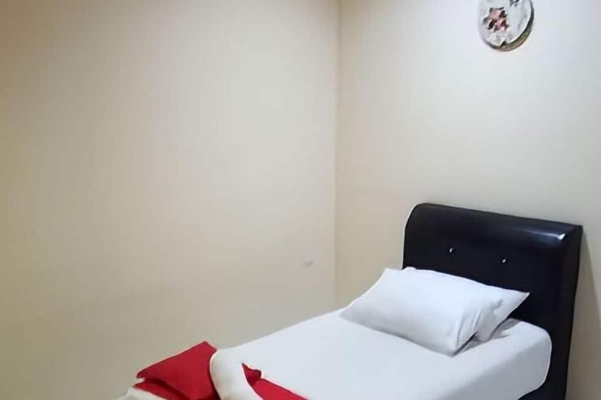 A small, single-bed room with a black headboard, white bedding, and a red accent on the bedspread.