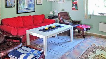 A living room with a red sofa, a white coffee table, a brown leather armchair, and a patterned rug.