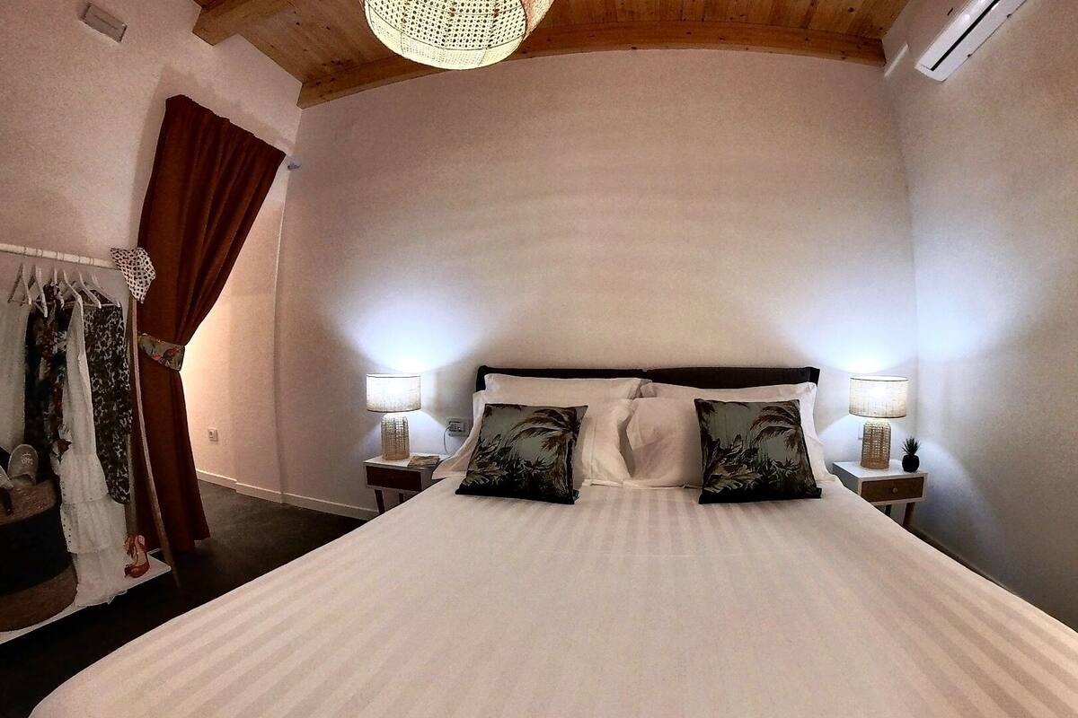 Quarto com cama grande, duas mesas de cabeceira com abajures, guarda-roupa e luminária pendente.