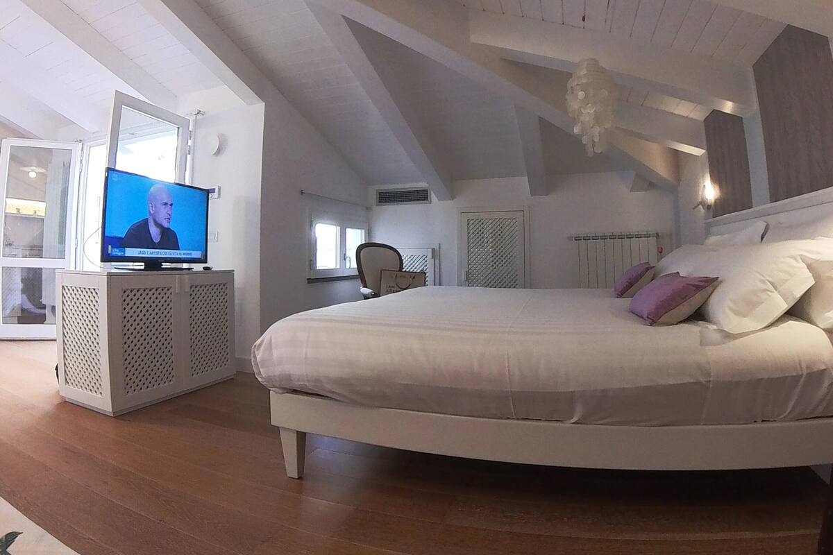 Quarto com uma cama grande, uma televisão sobre um móvel e uma janela.