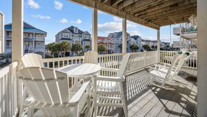 A covered outdoor area with white chairs and a table, overlooking a row of houses with balconies. - JUST UPDATED DEC '25!  4 br 4 ba ocean view villa- 16 steps to beach- pool club-directly across from beach access<br>Golf cart friendly. community pickle ball, tennis and basketball (Ocean Isle Beach)