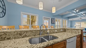 A kitchen with granite countertops, a double sink, wooden cabinets, and pendant lighting. - JUST UPDATED DEC '25!  4 br 4 ba ocean view villa- 16 steps to beach- pool club-directly across from beach access<br>Golf cart friendly. community pickle ball, tennis and basketball (Ocean Isle Beach)