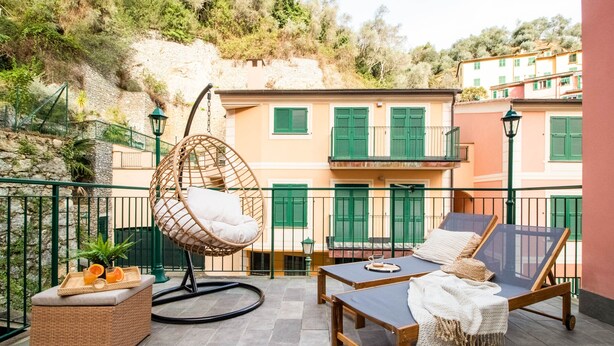 Un balcon agrémenté de meubles en osier, d’un fauteuil suspendu et d’une table sur laquelle se trouve un plateau d’oranges.