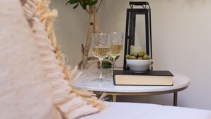 Une table ronde recouverte d’une nappe blanche, deux verres transparents, un bol d’olives vertes, un livre et une lanterne noire.