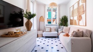 Un salon moderne doté d’un téléviseur à écran plat, d’un canapé, d’une table basse avec des collations, d’un lampadaire et d’une grande fenêtre offrant une vue sur les immeubles.