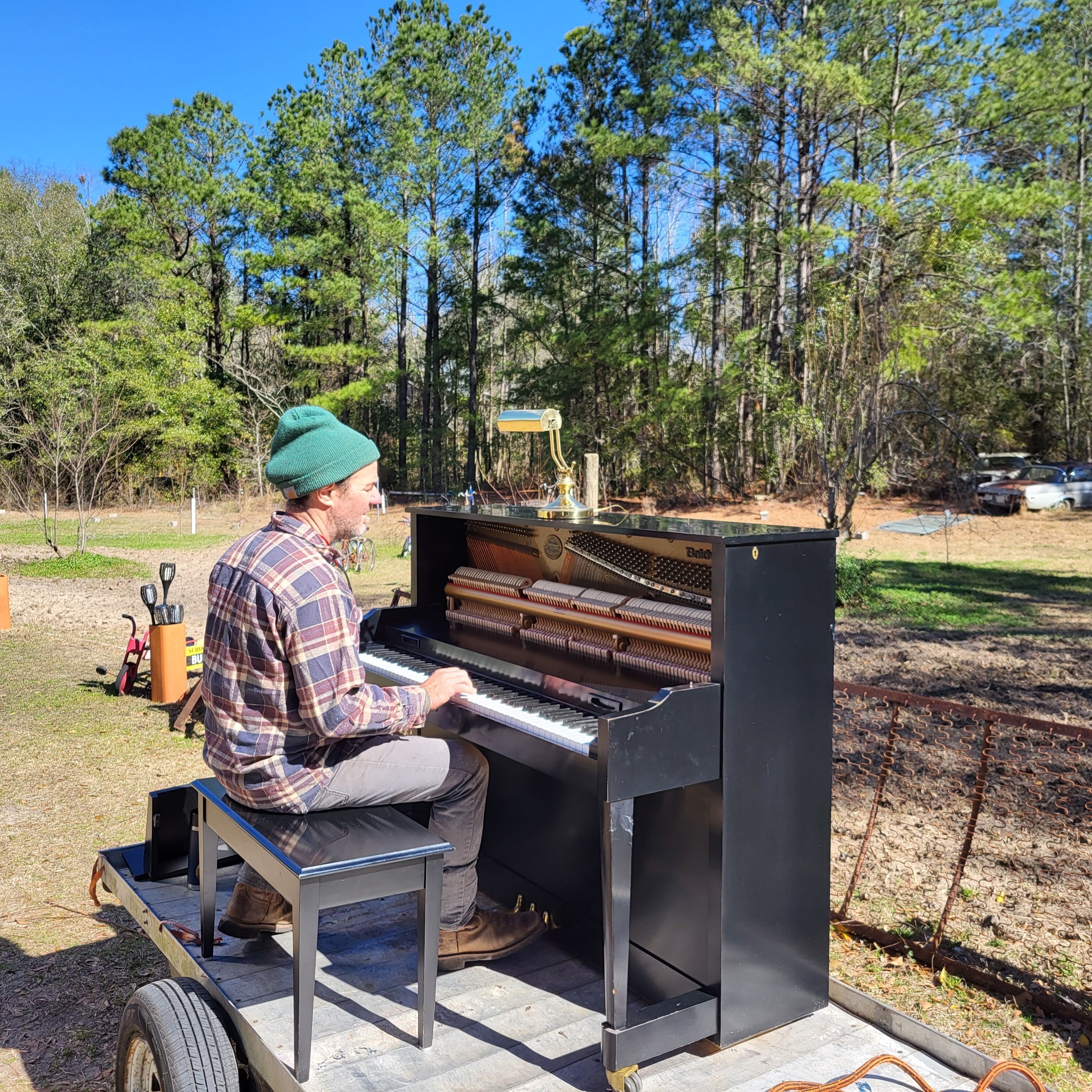 Una persona tocando un piano portátil al aire libre, con árboles y cielo despejado.