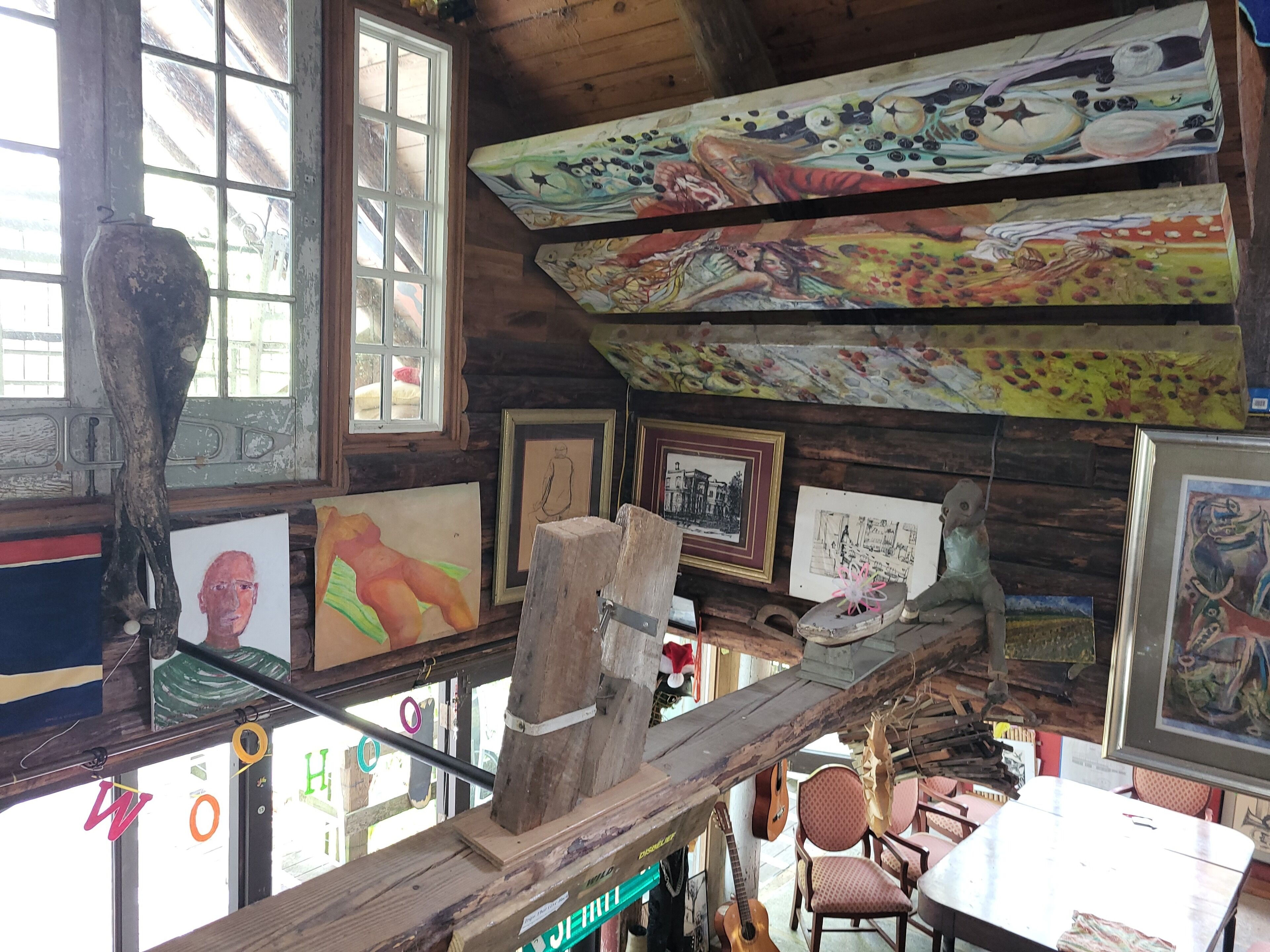 A rustic cabin interior with wooden walls, a loft bed, and various artworks displayed on the walls and shelves.